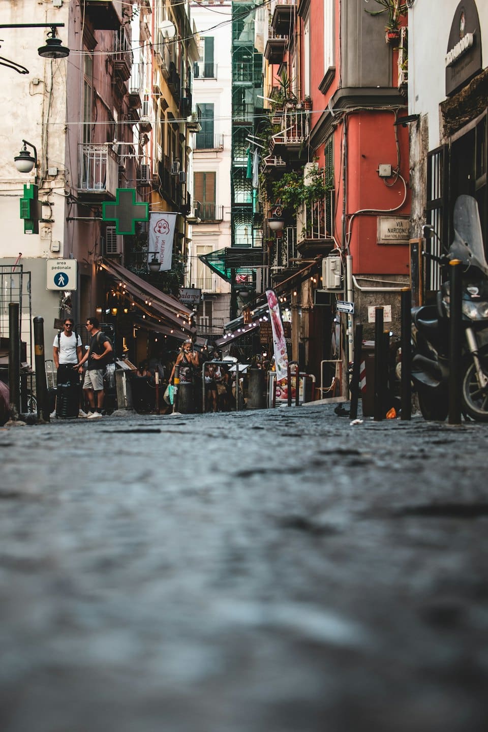 Pedestrians walk through a narrow historic European alleyway with shops.
