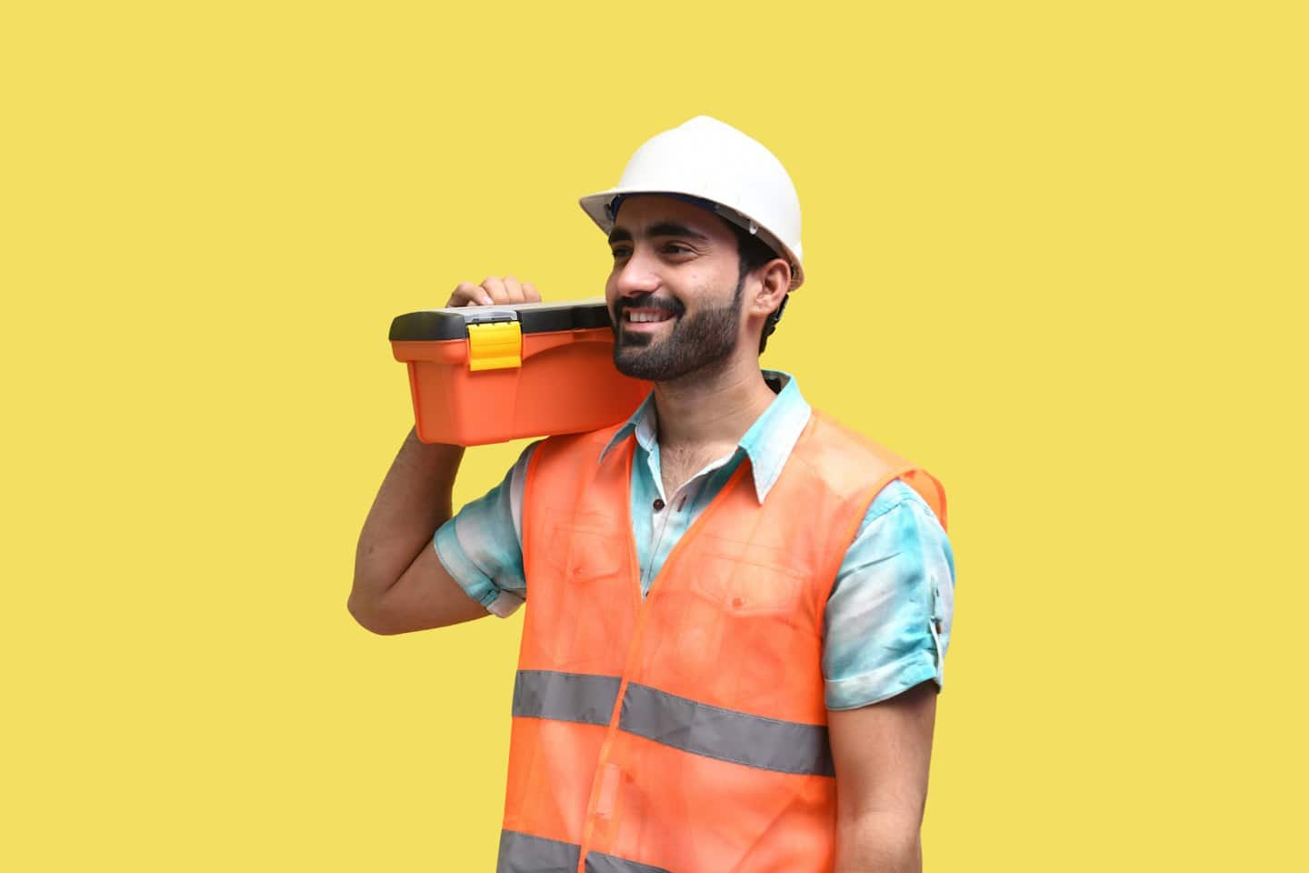 Man in hard hat and safety vest carries toolbox.